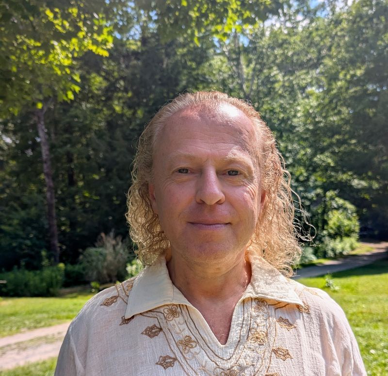 Sergio smiling outdoors in a cream embroidered shirt, with trees and a garden behind him