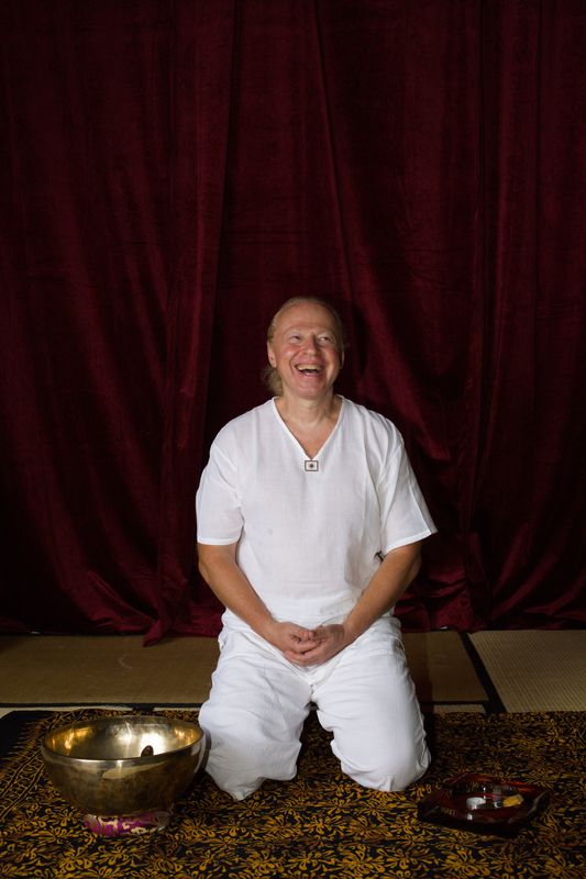 Sergio laughing as he kneels in white clothing, with a large brass bowl on the mat in front of him