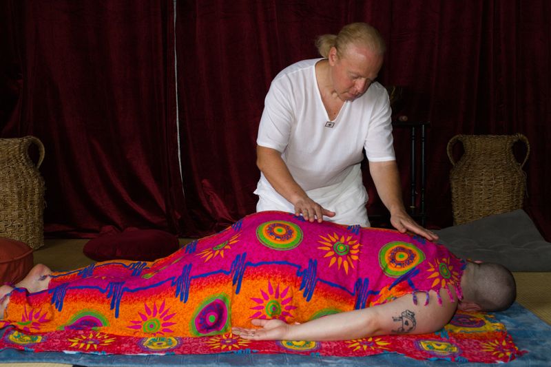 Sergio resting his hands on the back of a client who lies face down under a bright orange and pink sarong